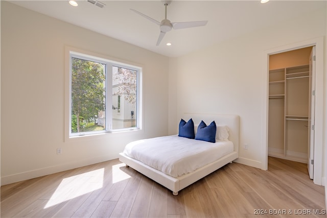 bedroom with ceiling fan, light wood-type flooring, multiple windows, and a walk in closet