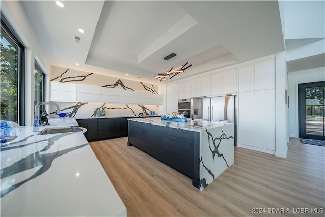 kitchen featuring backsplash, light hardwood / wood-style floors, stainless steel fridge, a raised ceiling, and a center island with sink