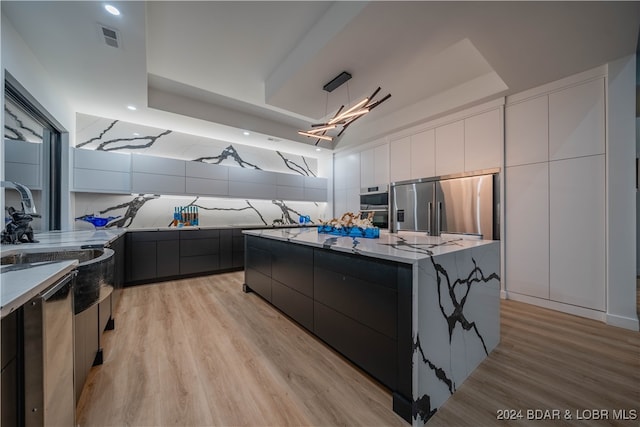 kitchen featuring hanging light fixtures, stainless steel appliances, light hardwood / wood-style floors, sink, and a center island with sink