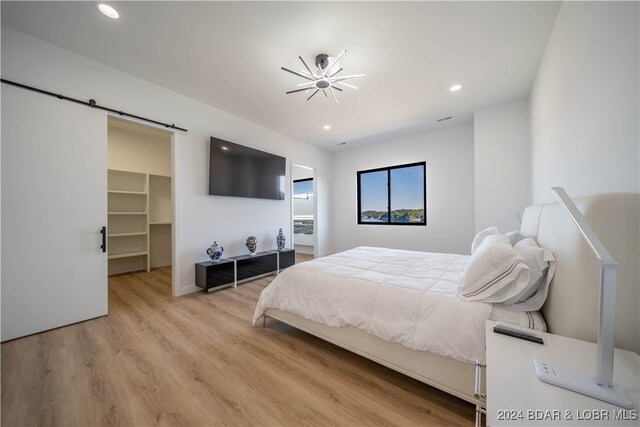 bedroom with light wood-type flooring, a walk in closet, a barn door, and a closet