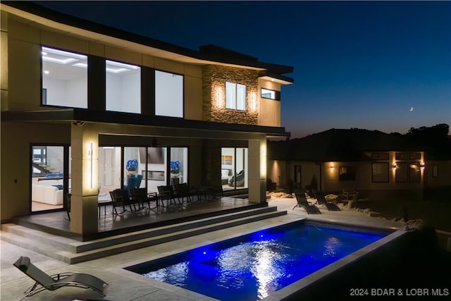 back house at night featuring a patio area and a swimming pool with hot tub