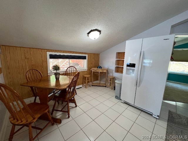 dining room with lofted ceiling, light tile patterned floors, wood walls, and a textured ceiling