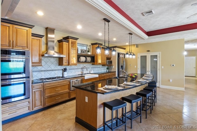 kitchen featuring stainless steel appliances, sink, wall chimney range hood, a kitchen bar, and a center island with sink