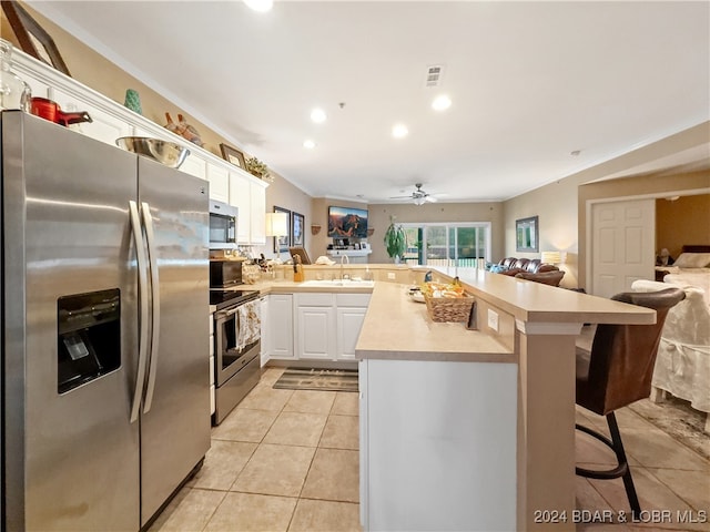 kitchen with kitchen peninsula, appliances with stainless steel finishes, a breakfast bar, white cabinetry, and crown molding