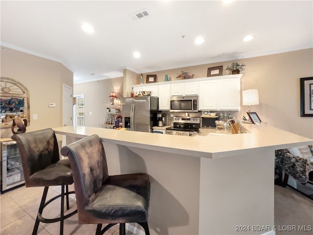 kitchen featuring kitchen peninsula, appliances with stainless steel finishes, a breakfast bar, white cabinetry, and crown molding