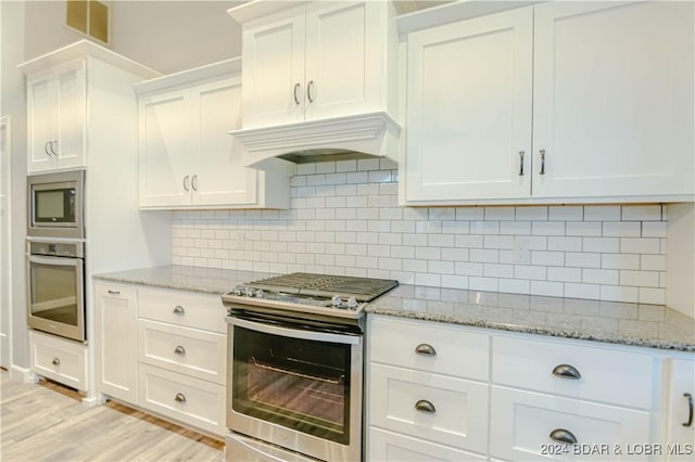 kitchen with stainless steel appliances, white cabinetry, custom range hood, and tasteful backsplash