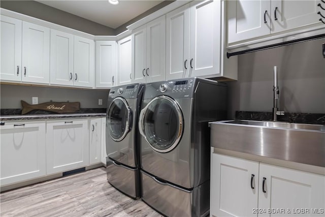 laundry area featuring cabinets, independent washer and dryer, sink, and light hardwood / wood-style flooring