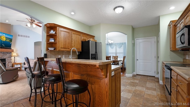 kitchen with kitchen peninsula, stainless steel appliances, a breakfast bar, and ceiling fan with notable chandelier