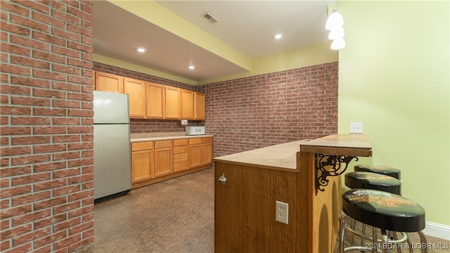 kitchen featuring brick wall, kitchen peninsula, a kitchen breakfast bar, carpet flooring, and white fridge