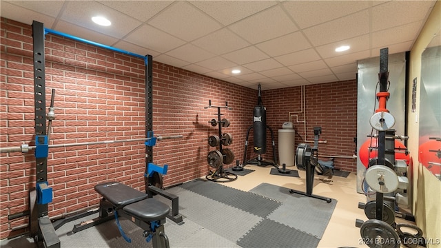 exercise room with a paneled ceiling and brick wall