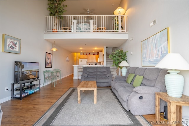 living room featuring ceiling fan, hardwood / wood-style flooring, and a towering ceiling