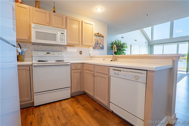 kitchen with lofted ceiling, kitchen peninsula, white appliances, and light hardwood / wood-style floors