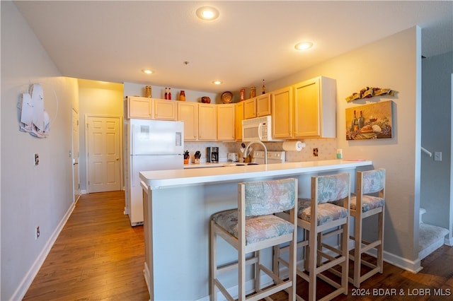 kitchen featuring white appliances, a breakfast bar, kitchen peninsula, and light hardwood / wood-style flooring