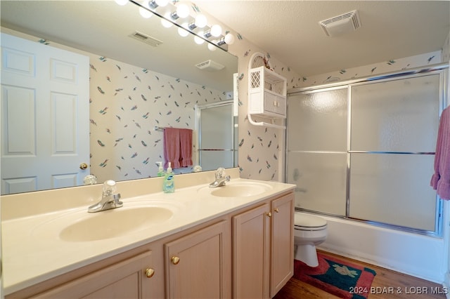 full bathroom with hardwood / wood-style flooring, a textured ceiling, toilet, combined bath / shower with glass door, and vanity