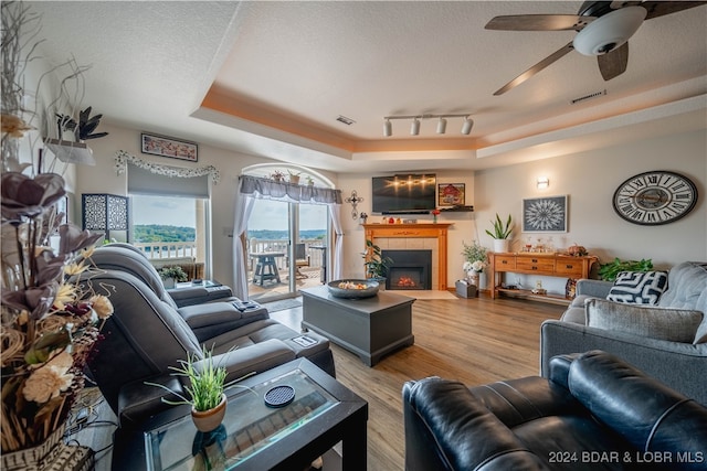 living room featuring a tile fireplace, hardwood / wood-style flooring, a tray ceiling, ceiling fan, and a textured ceiling