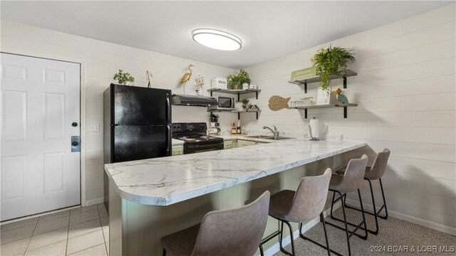 kitchen with kitchen peninsula, a kitchen bar, sink, black appliances, and light tile patterned floors