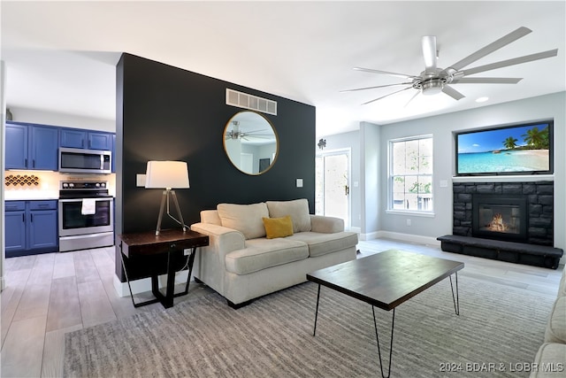 living room with ceiling fan, a stone fireplace, and light wood-type flooring