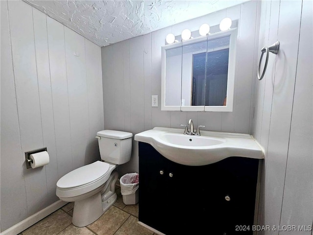 bathroom featuring a textured ceiling, vanity, toilet, tile patterned floors, and wooden walls