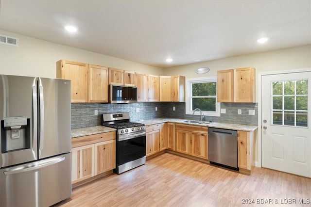 kitchen featuring light wood-type flooring, light stone countertops, stainless steel appliances, and sink