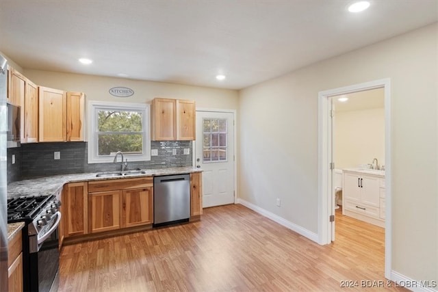 kitchen featuring tasteful backsplash, sink, light stone countertops, appliances with stainless steel finishes, and light hardwood / wood-style floors