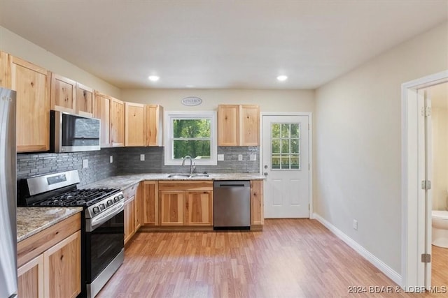 kitchen with light brown cabinetry, tasteful backsplash, stainless steel appliances, and light wood-type flooring