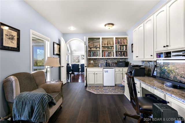 kitchen featuring white dishwasher, built in desk, light stone counters, and dark wood-type flooring