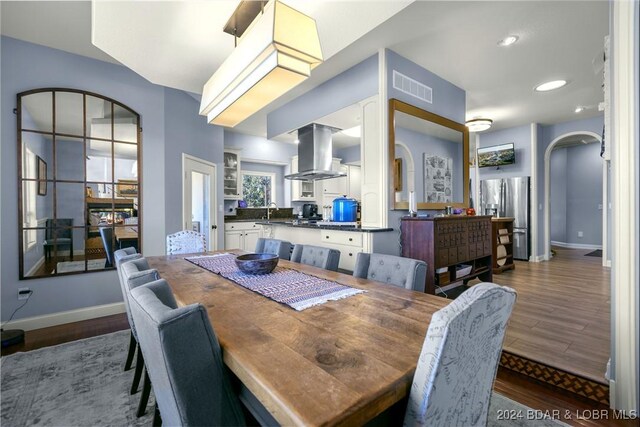 dining space featuring arched walkways, dark wood-type flooring, visible vents, and baseboards