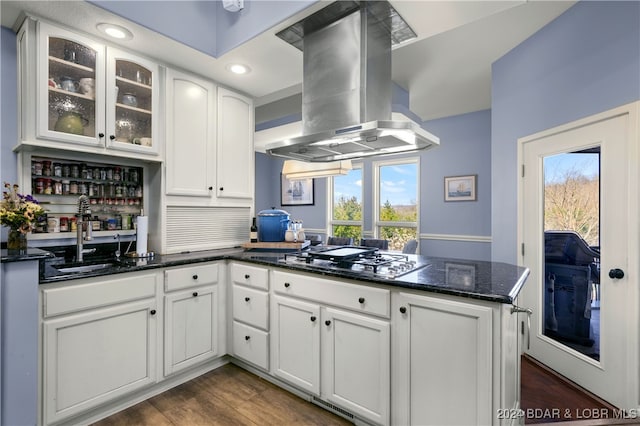 kitchen featuring stainless steel gas cooktop, island exhaust hood, sink, dark stone countertops, and white cabinets