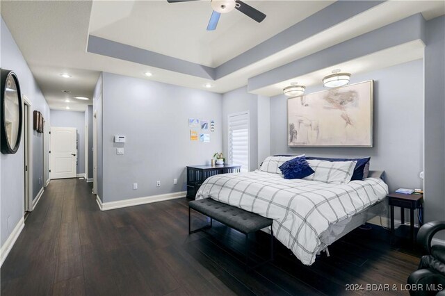 bedroom featuring recessed lighting, a tray ceiling, dark wood-type flooring, and baseboards