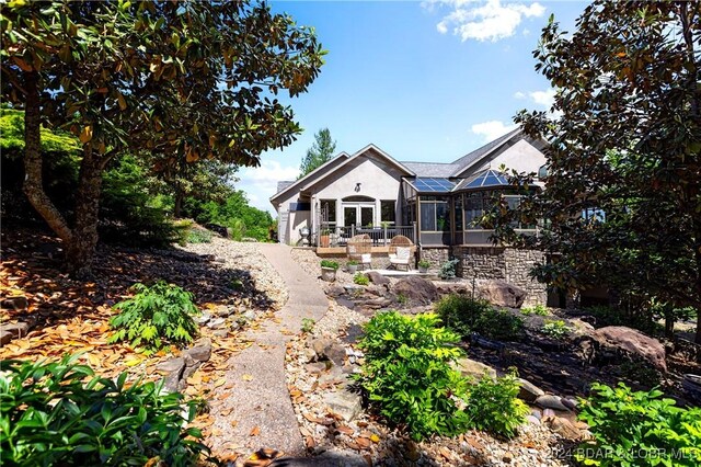 rear view of house with a sunroom, stucco siding, and stone siding