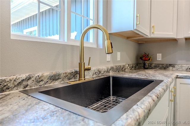 details with white cabinets, light stone counters, and sink