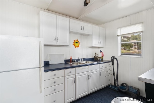 kitchen with white cabinets, white refrigerator, wood walls, and sink