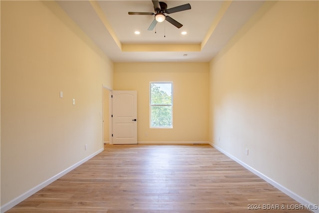 empty room featuring a tray ceiling, ceiling fan, and light hardwood / wood-style flooring