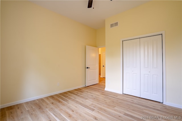 unfurnished bedroom with ceiling fan, a closet, light hardwood / wood-style floors, and a high ceiling