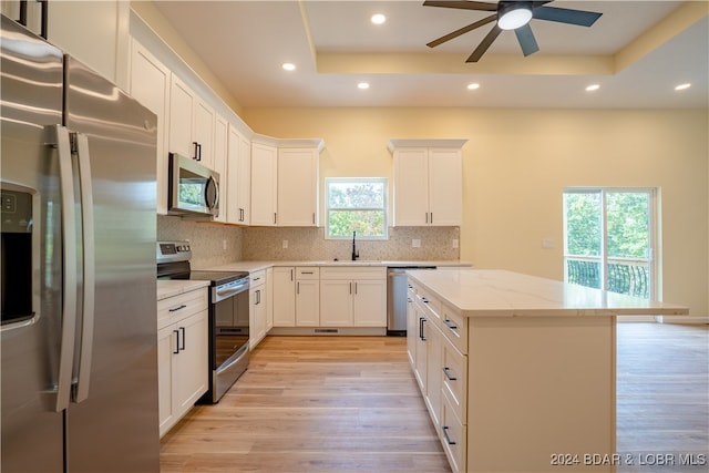 kitchen featuring a raised ceiling, light wood-type flooring, ceiling fan, and appliances with stainless steel finishes