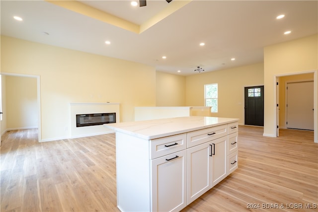 kitchen with light hardwood / wood-style flooring, white cabinets, light stone counters, and a kitchen island