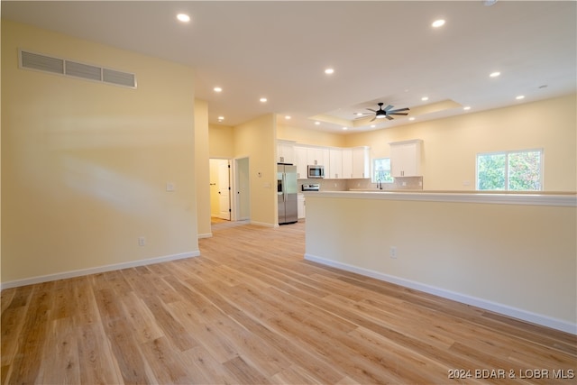 interior space featuring ceiling fan, light wood-type flooring, and a tray ceiling