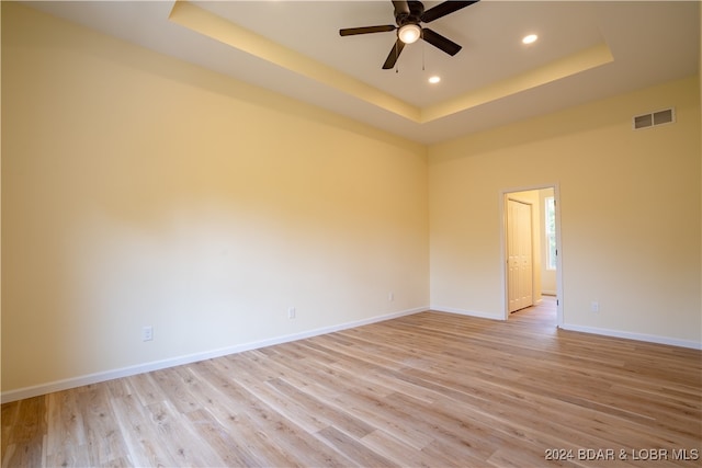 empty room with ceiling fan, a tray ceiling, and light hardwood / wood-style floors