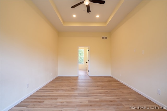 empty room with light wood-type flooring, a raised ceiling, and ceiling fan