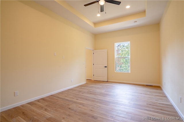 empty room with light wood-type flooring, a raised ceiling, and ceiling fan