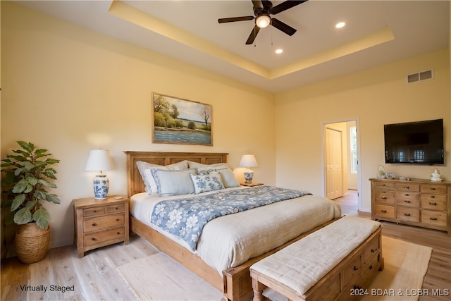 bedroom featuring ceiling fan, ensuite bathroom, a tray ceiling, and light hardwood / wood-style floors