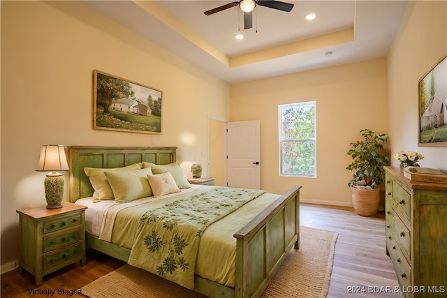 bedroom with wood-type flooring, a tray ceiling, and ceiling fan