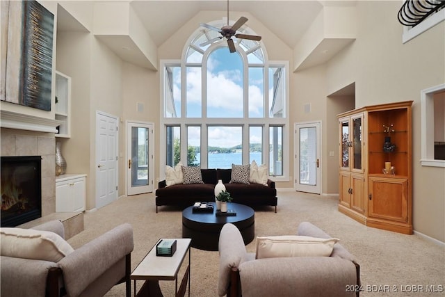 carpeted living room featuring a water view, ceiling fan, plenty of natural light, and a tile fireplace