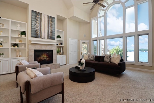 carpeted living room featuring ceiling fan, a high ceiling, a tile fireplace, and a wealth of natural light