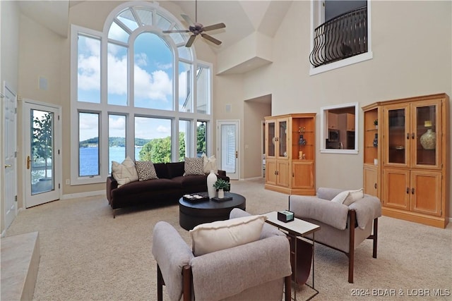 living room with a water view, ceiling fan, light carpet, and a high ceiling