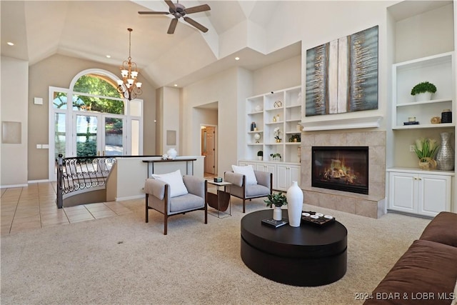 carpeted living room featuring a tiled fireplace, built in shelves, ceiling fan with notable chandelier, and high vaulted ceiling