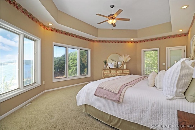 carpeted bedroom featuring ceiling fan, a tray ceiling, and multiple windows