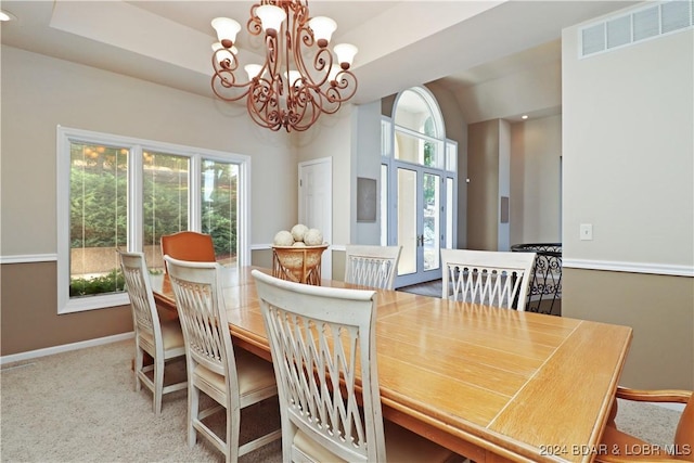 carpeted dining room featuring a raised ceiling and an inviting chandelier