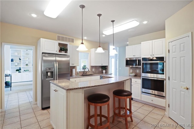 kitchen with stainless steel appliances, white cabinetry, light stone countertops, and a center island