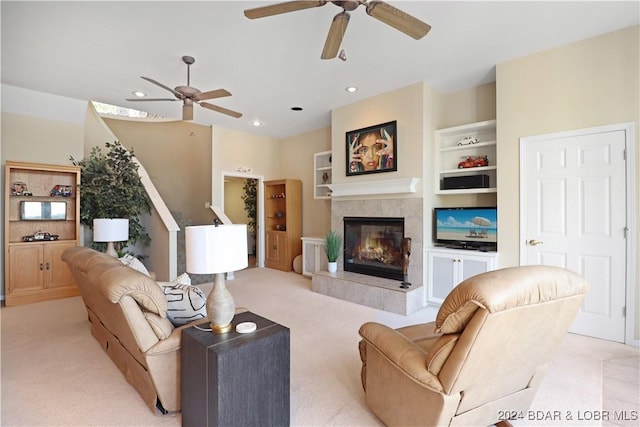 living room with built in features, a fireplace, light colored carpet, and ceiling fan